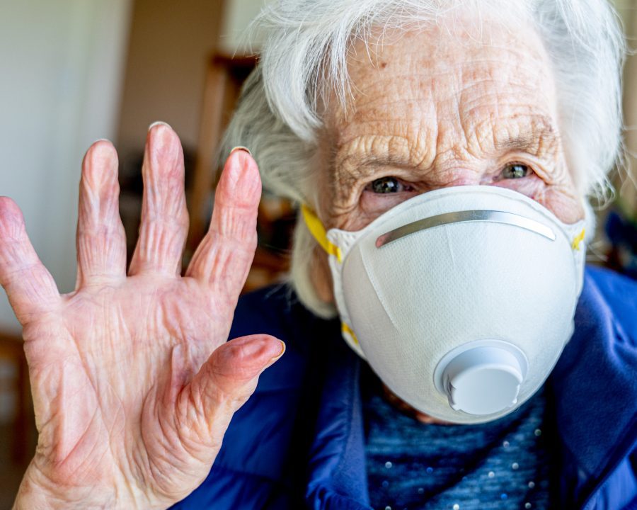 Close-Up Shot of Elderly Senior Caucasian Woman Smiling Holding Her Hands Up Waving Hello or Goodbye Wearing an n95 Protective Face Mask To Prevent the Spread of COVID SARS nCoV 19 Coronavirus Swine Flu H7N9 Influenza Illness During Cold and Flu Season