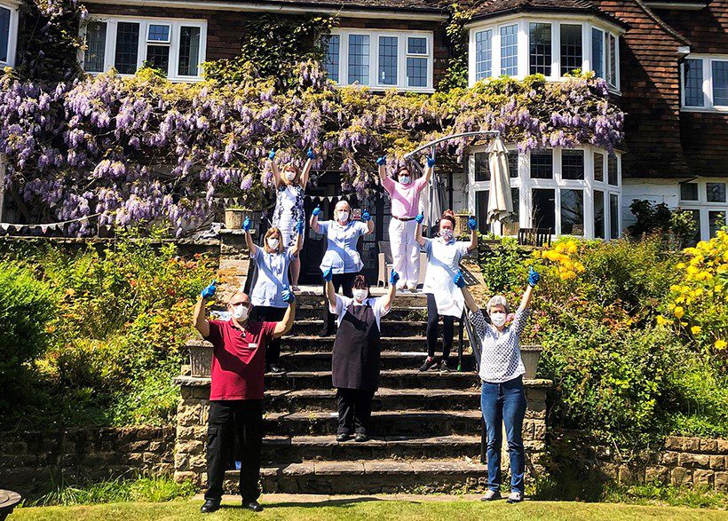 Staff on the care home's steps giving thumbs up. 