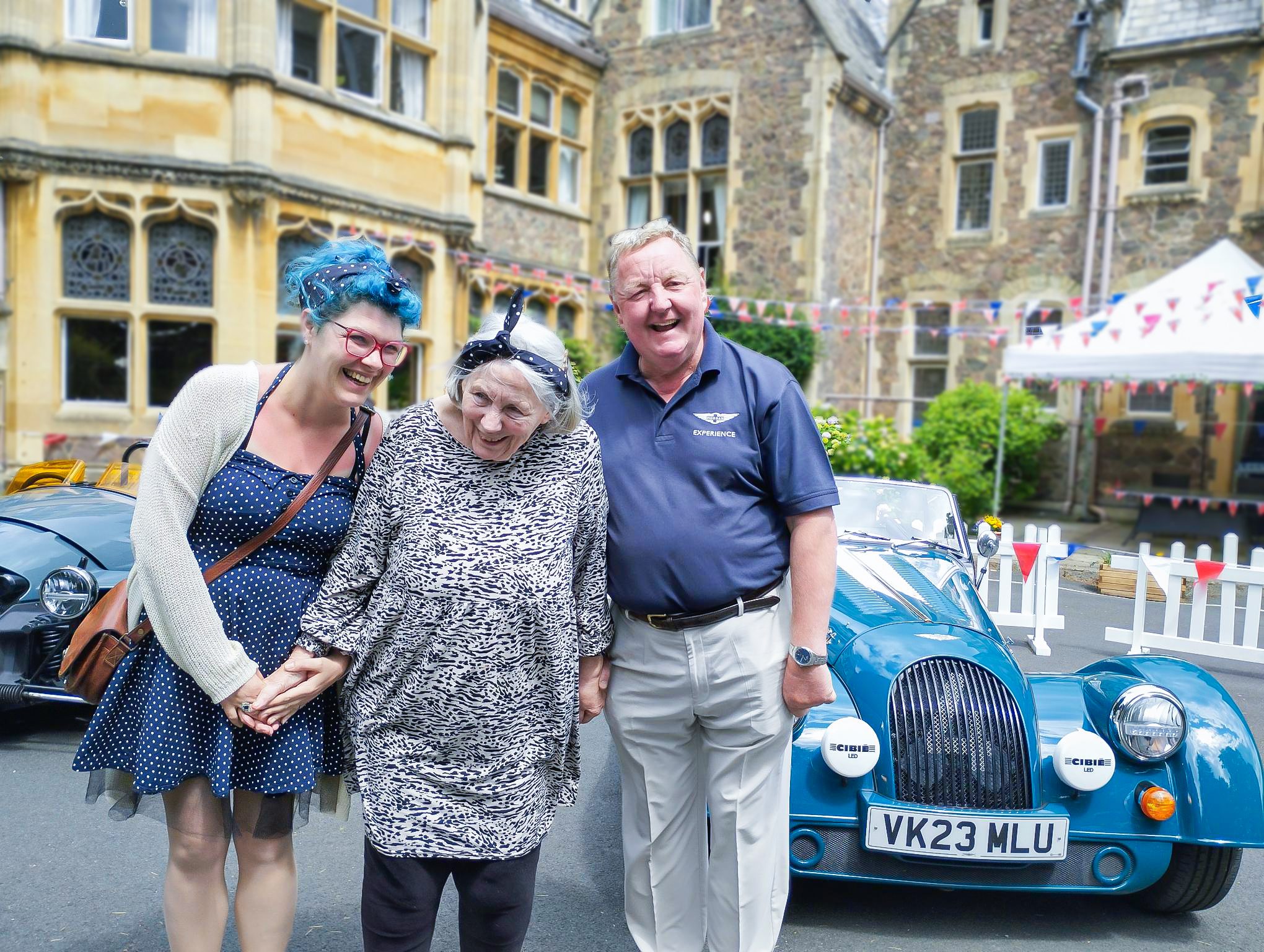A resident and staff members alongside classic cars.
