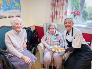 Two residents next to a chef holding a plate of mince pies.