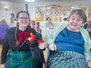 Burns Night bagpipe player sat with resident. 