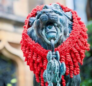 A close up of the lion on the well wearing a knitted mane.