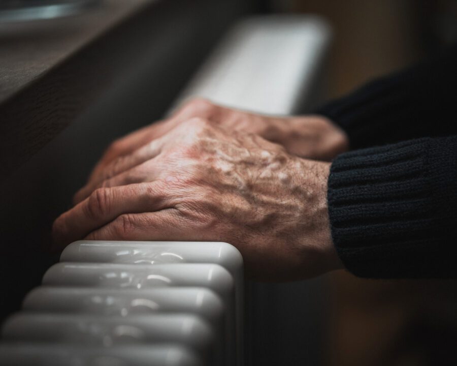 Cold at home. A man tries to warm his hands on a radiator